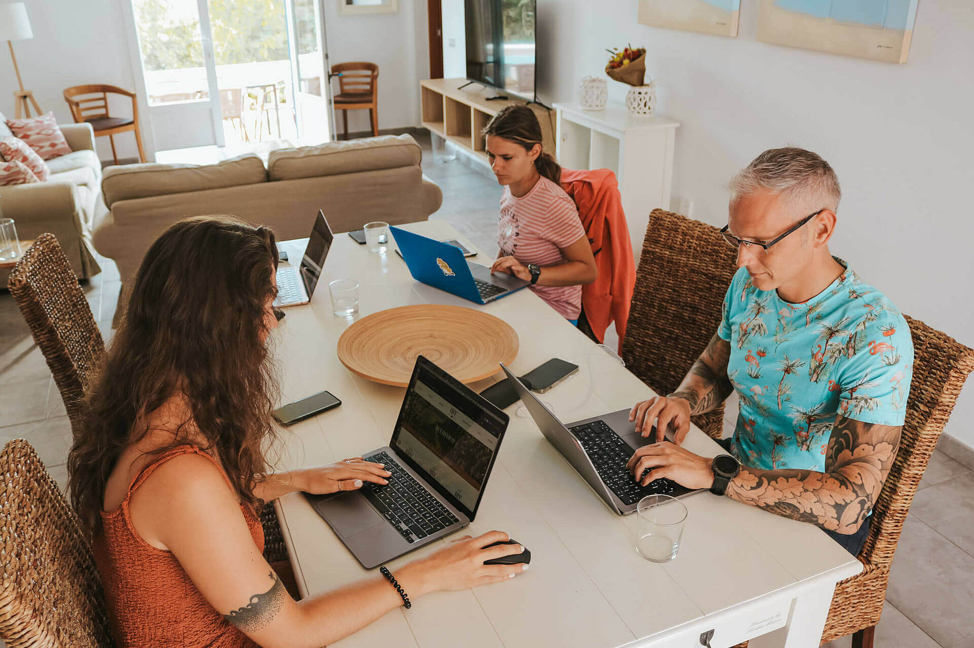 Drei Menschen arbeiten gemeinsam an Laptops in einem modernen Wohnzimmer. Zusammenarbeit im Homeoffice.