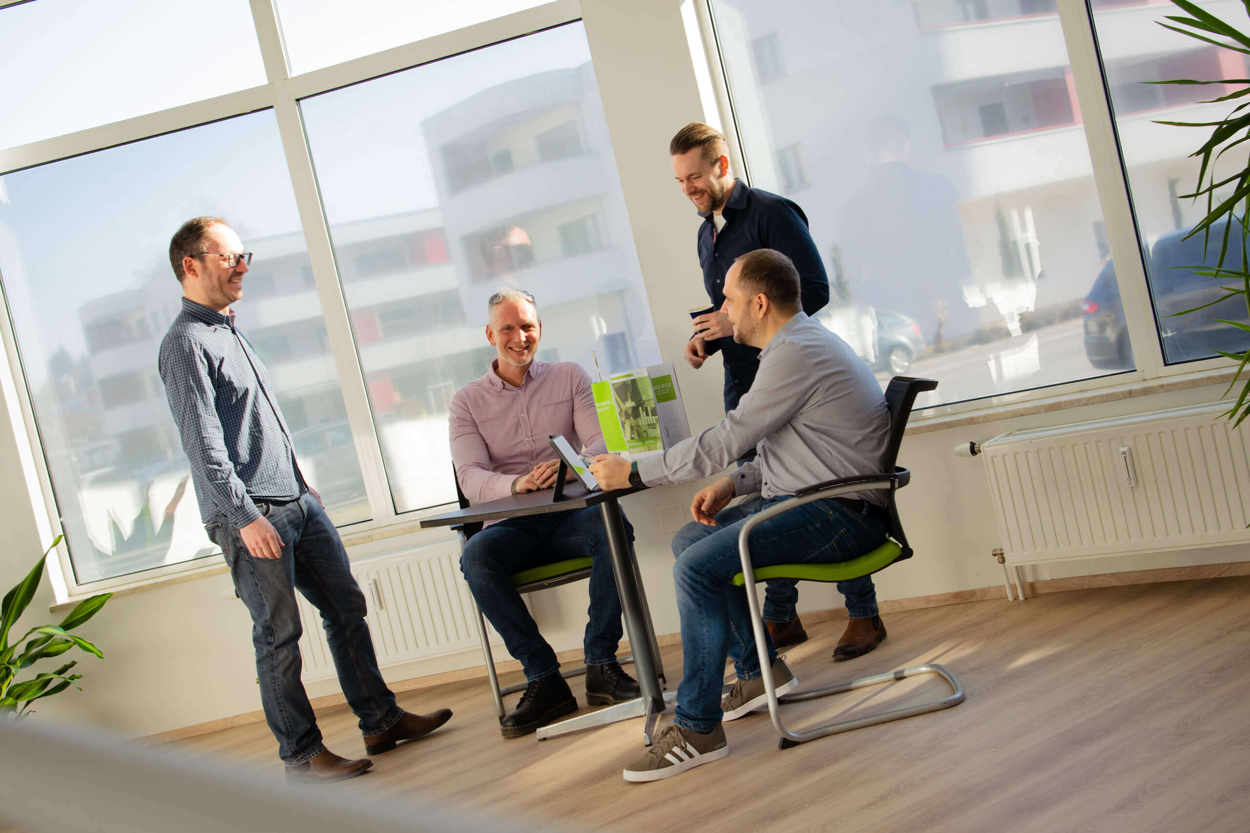 Gruppe von vier Männern in einem hellen Büro beim Meeting, lächelnd und diskutierend um einen Tisch.