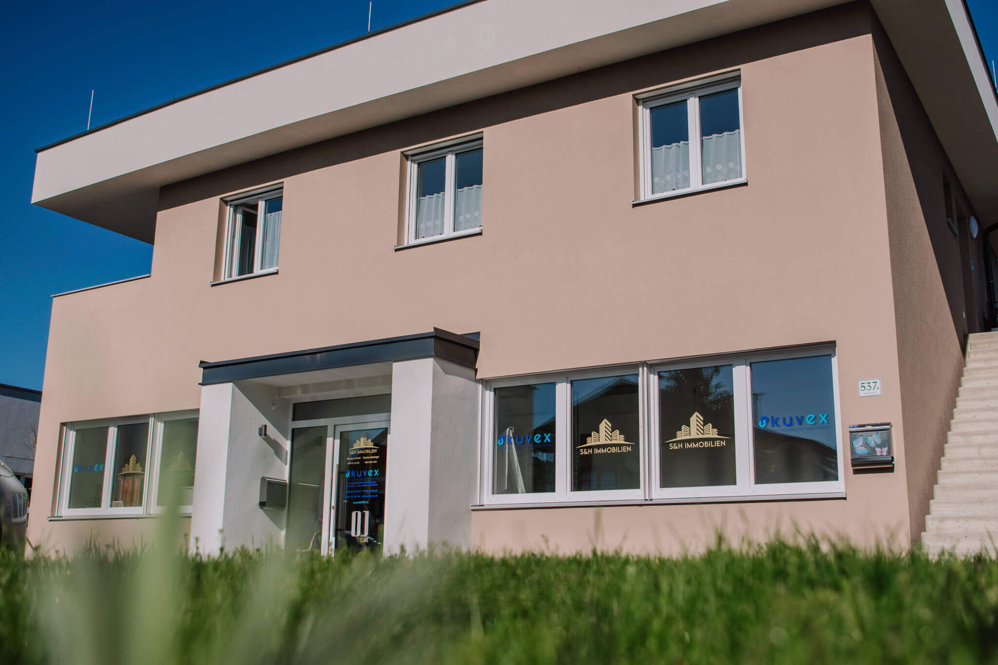 Modernes Bürogebäude von S&H Immobilien, umgeben von grüner Wiese und blauem Himmel.