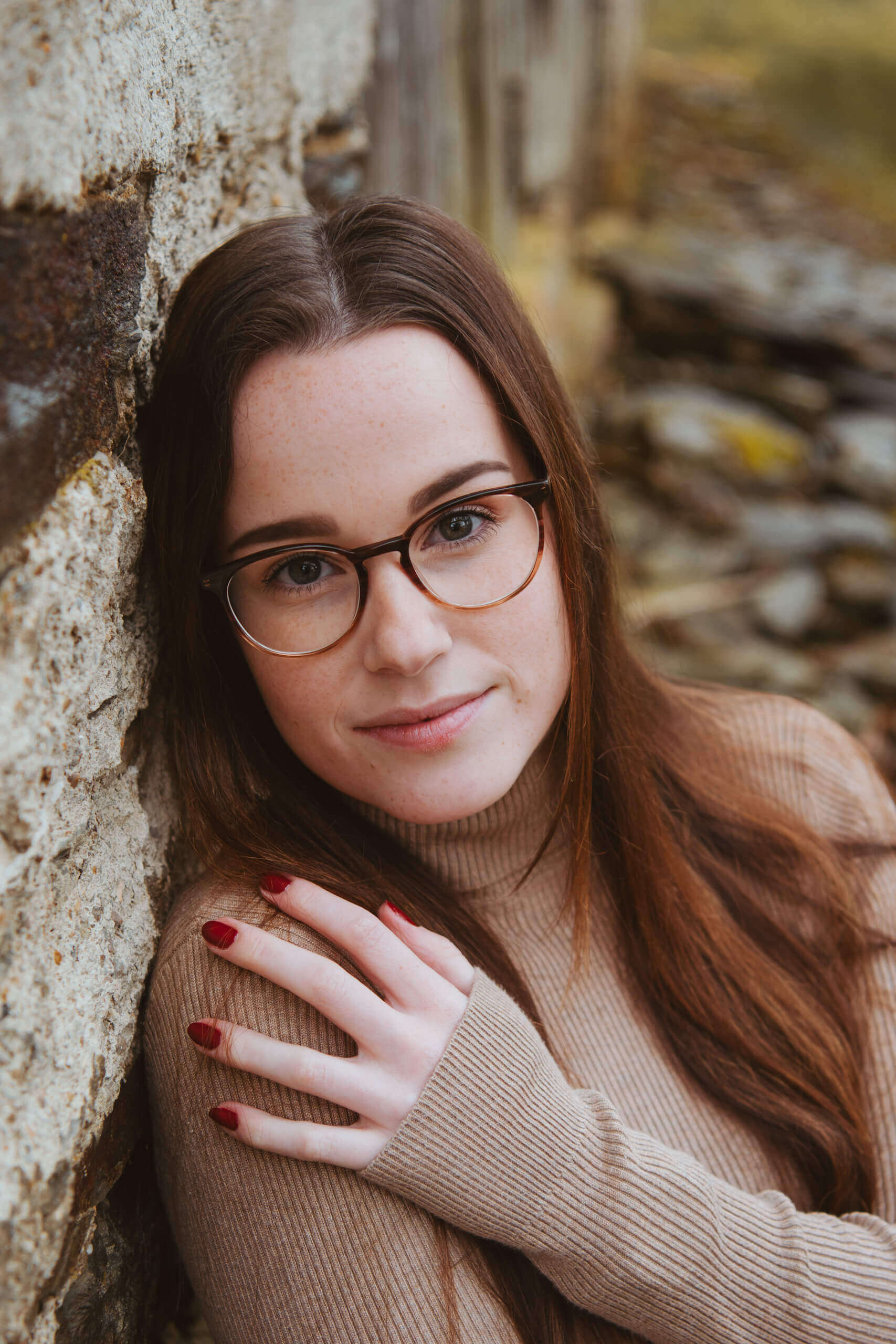 Frau mit Brille lehnt an Backsteinmauer und schaut in die Kamera. Vintage-Look.