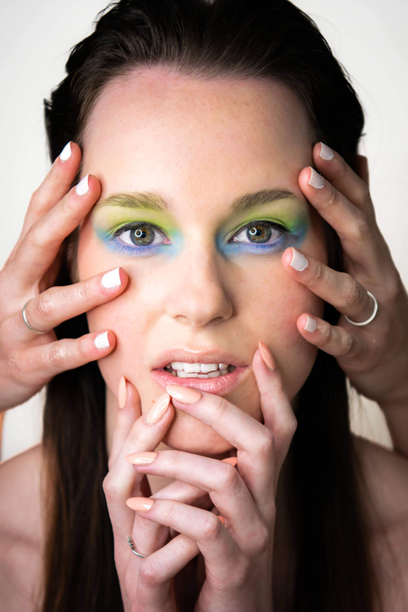 Frau mit farbenfrohem Augen-Make-up, umgeben von Händen mit modernem Nageldesign. Moderner, kreativer Look.