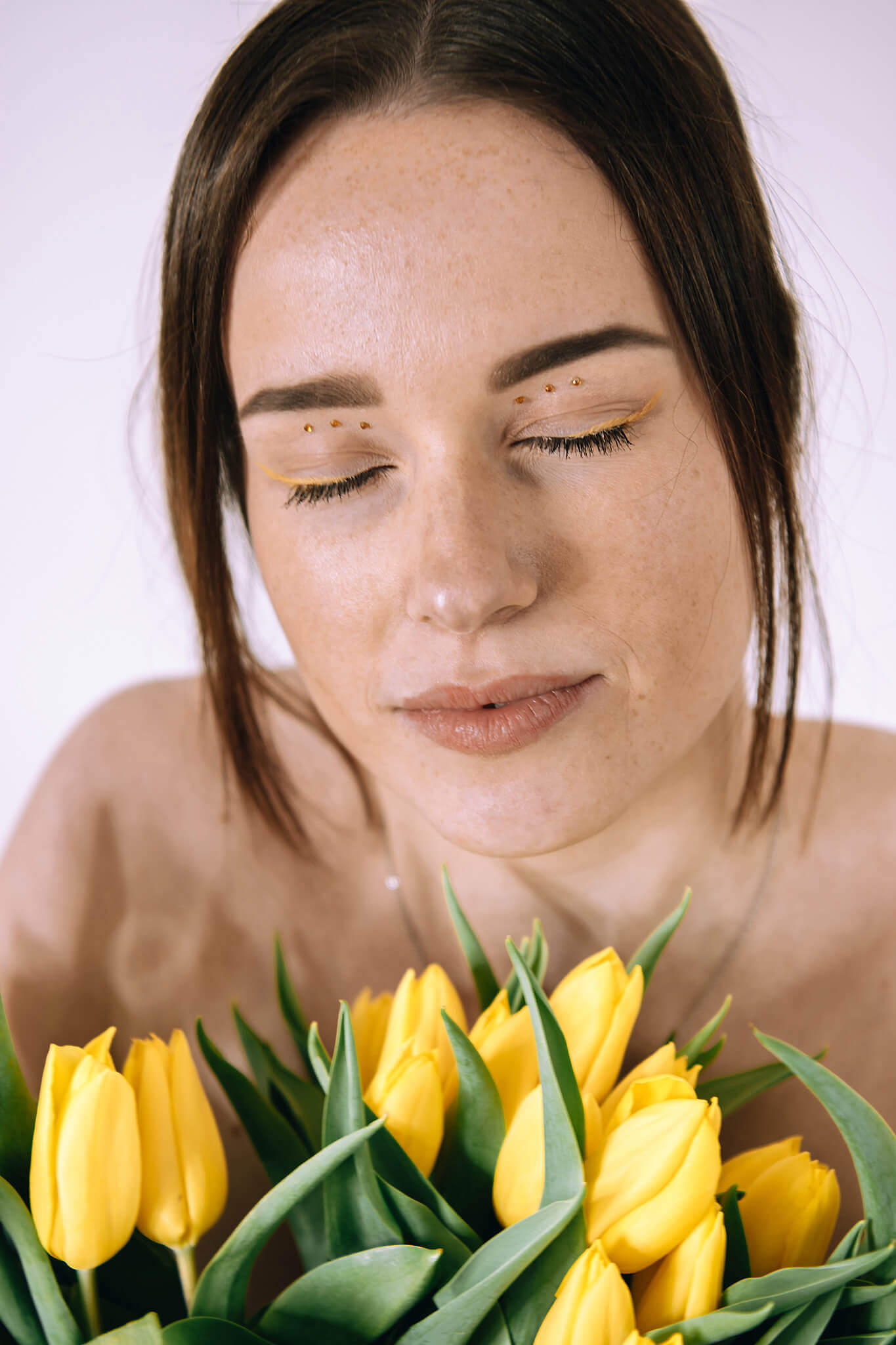 Frau mit geschlossenen Augen hält gelbe Tulpen in der Hand vor weißem Hintergrund. Frühlingsstimmung und Gelassenheit.