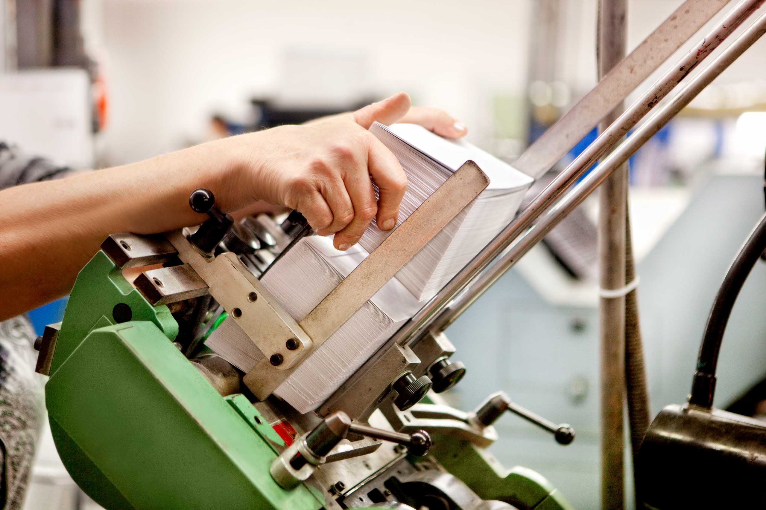 Druckmaschine in Aktion: Ein Stapel Papier wird von Hand in eine Druckmaschine eingelegt.