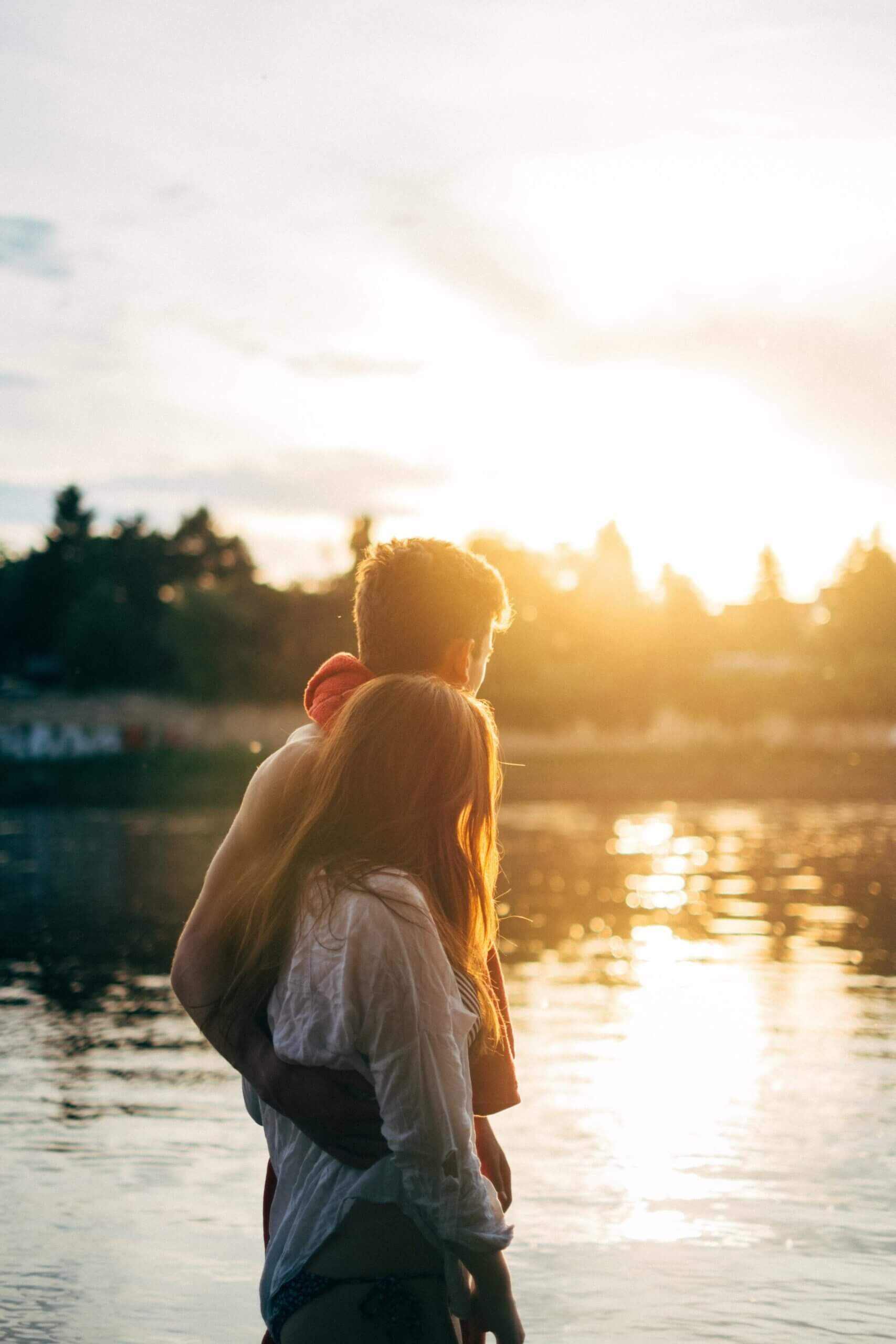 Pärchen am Flussufer bei Sonnenuntergang, romantische Stimmung in natürlicher Umgebung.