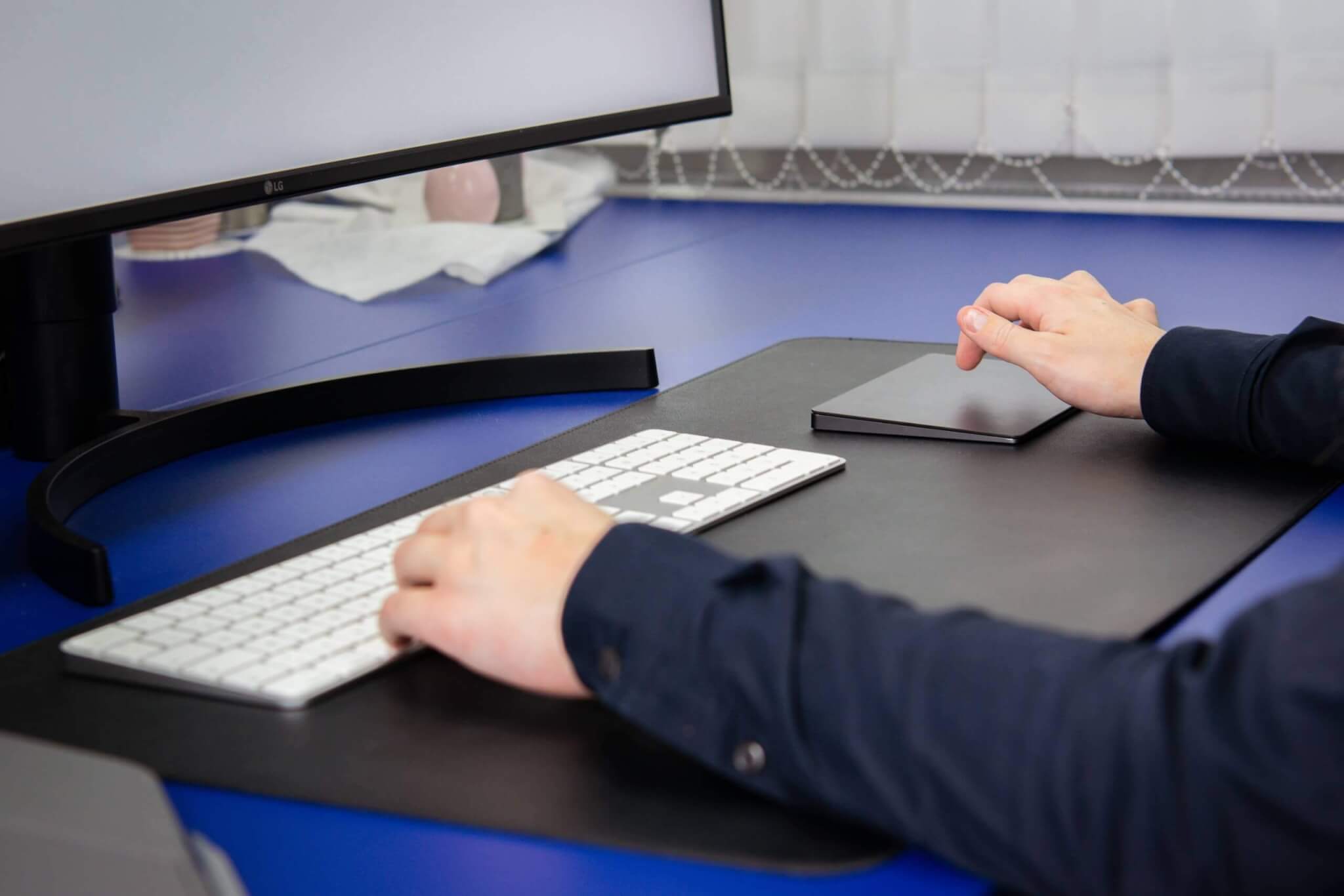 Person arbeitet an einem Schreibtisch mit Tastatur und Curved-Monitor, moderne Büroeinrichtung.