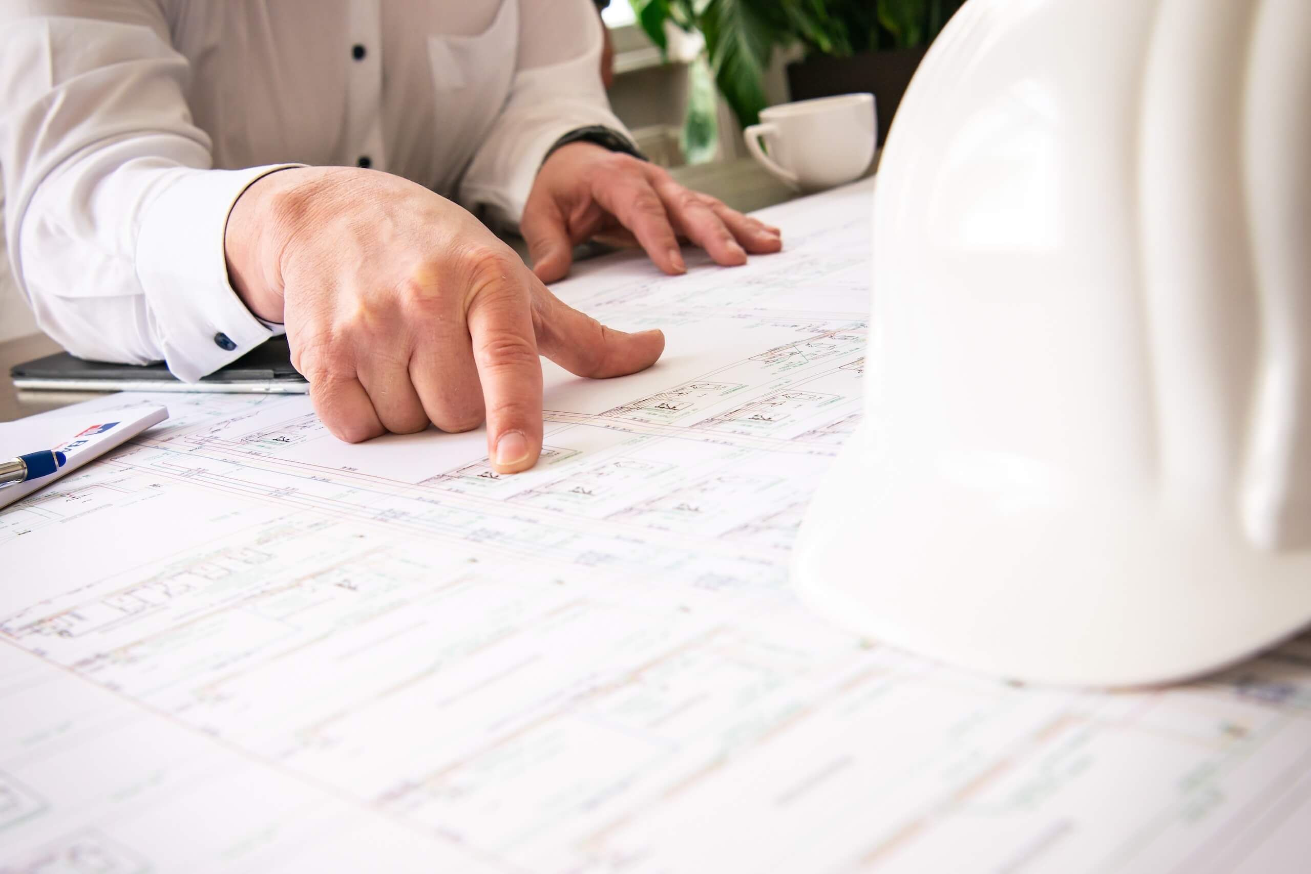 Architekt zeigt auf Bauplan mit Schutzhelm, Planung im Ingenieurbüro.