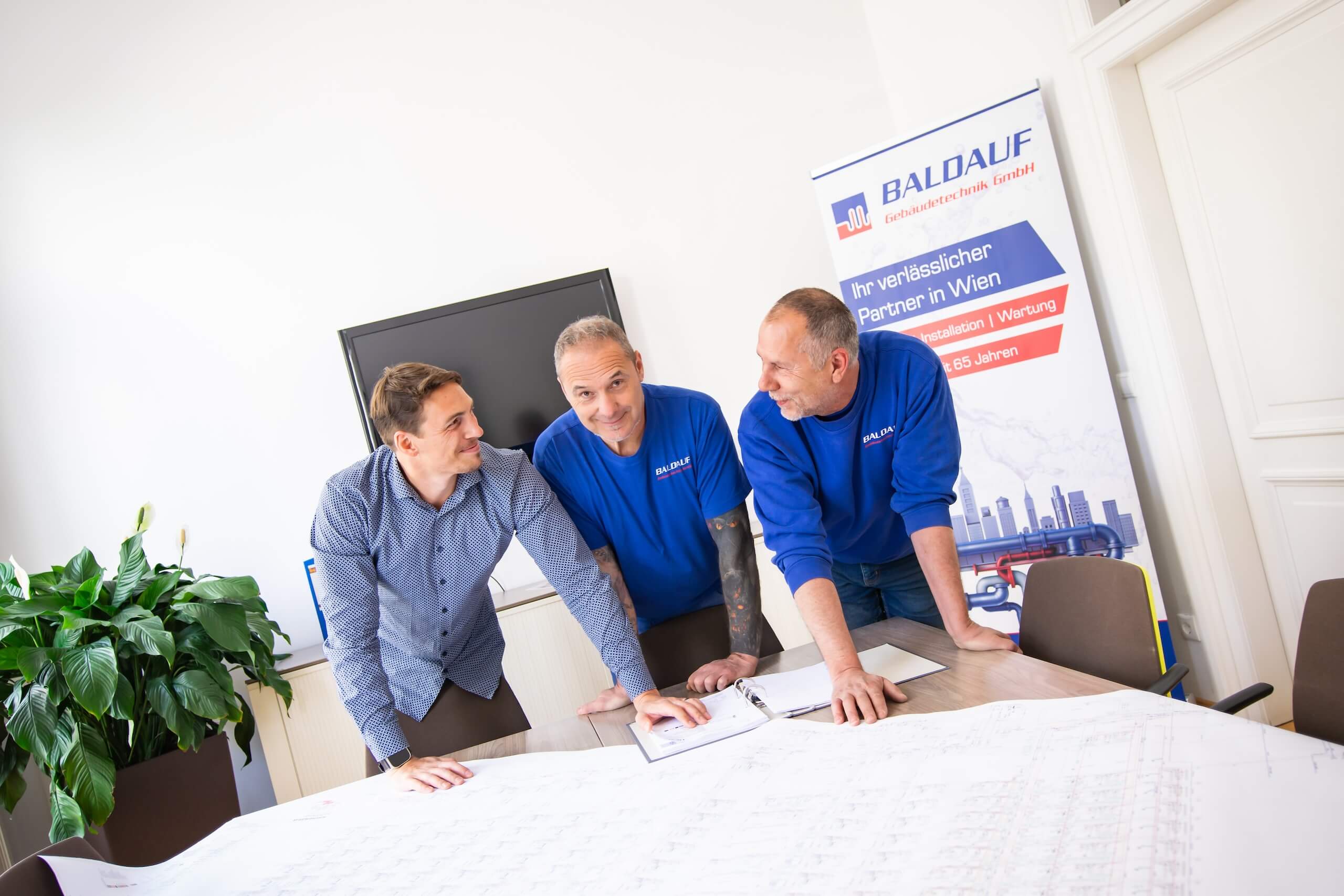 Drei Männer besprechen Baupläne im Büro von Baldauf Gebäudetechnik, Ihrem Partner für Installation und Wartung in Wien.