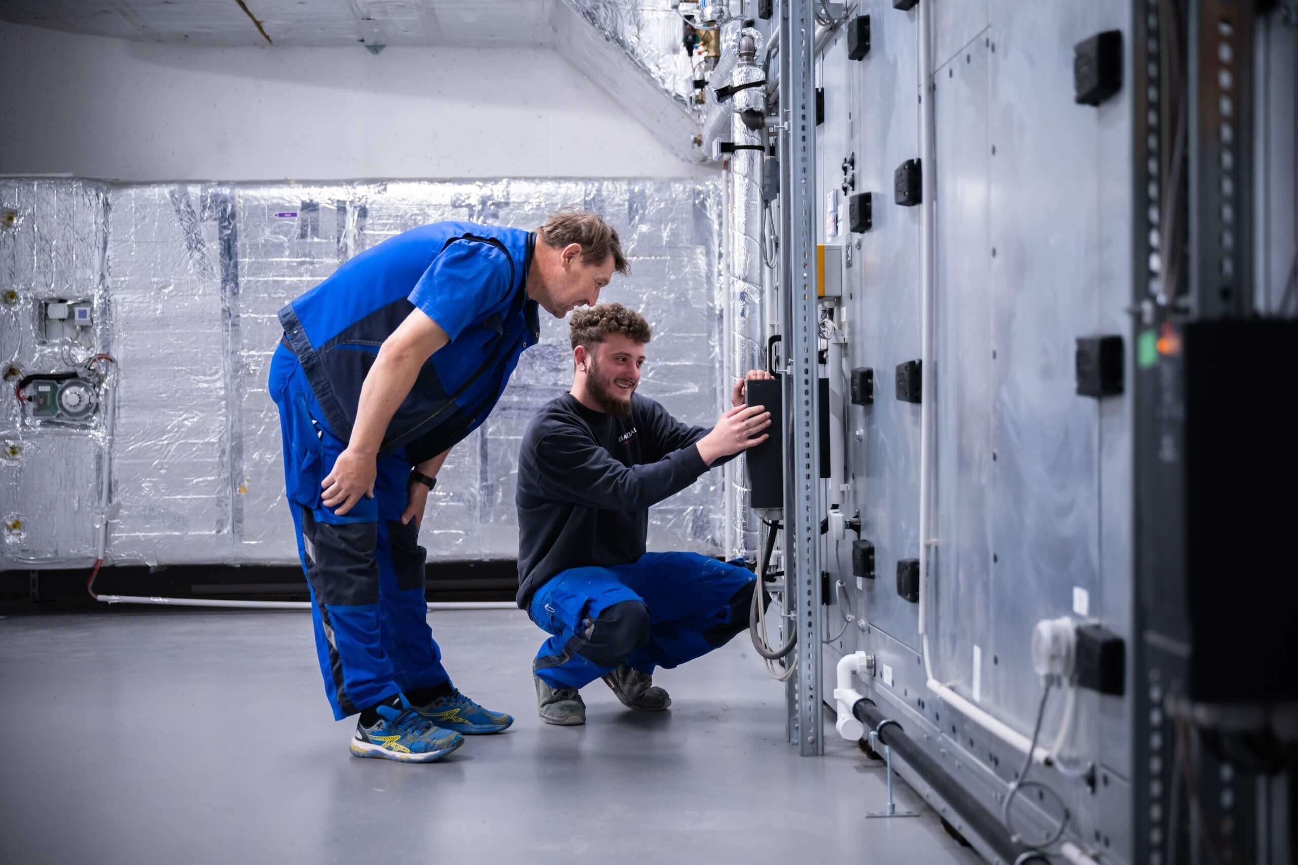 Zwei Techniker prüfen Lüftungsanlage im Industriegebäude für optimale Leistung und Wartung.