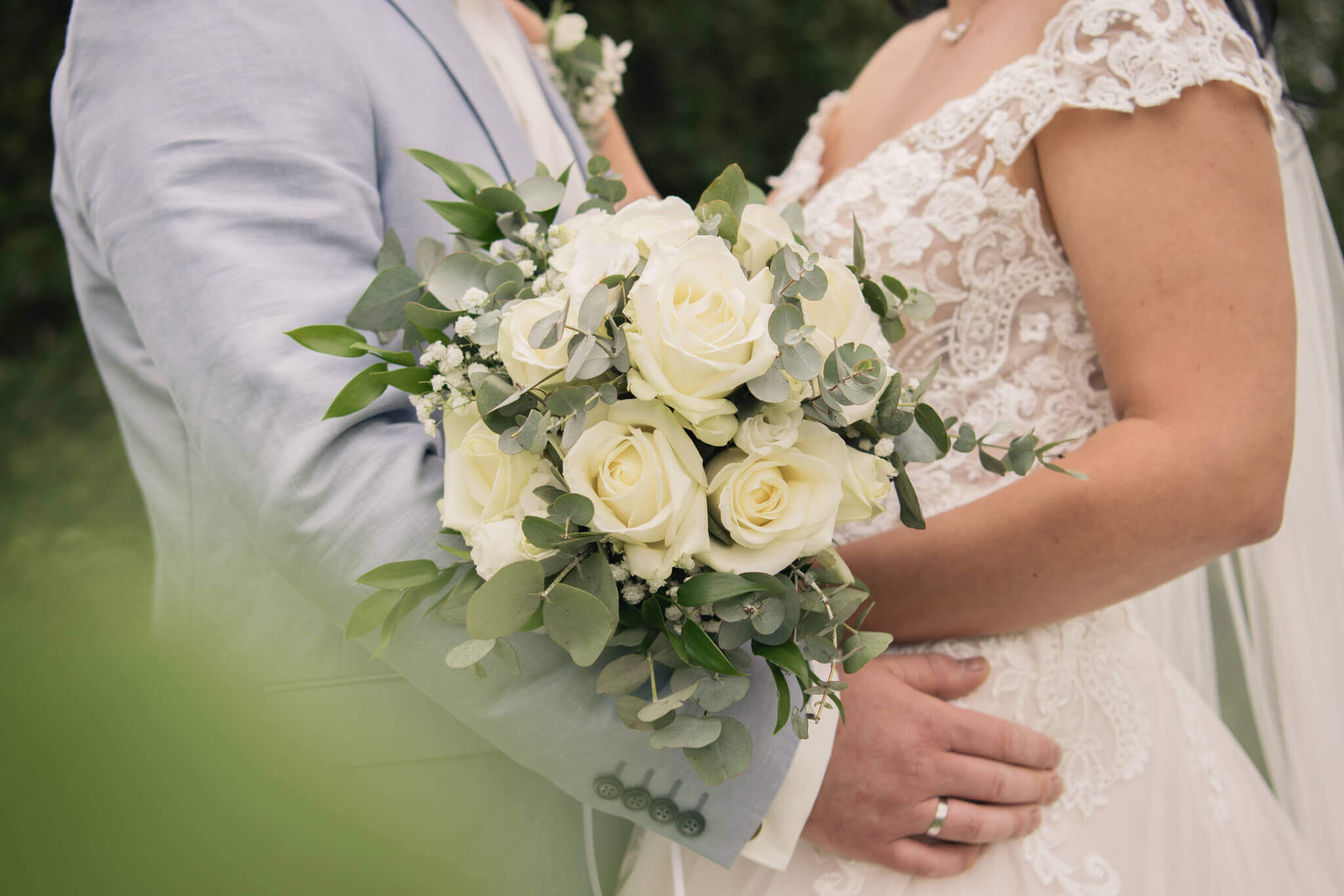 Brautpaar in eleganter Hochzeitskleidung mit einem weißen Rosenstrauß bei einer romantischen Outdoor-Zeremonie.