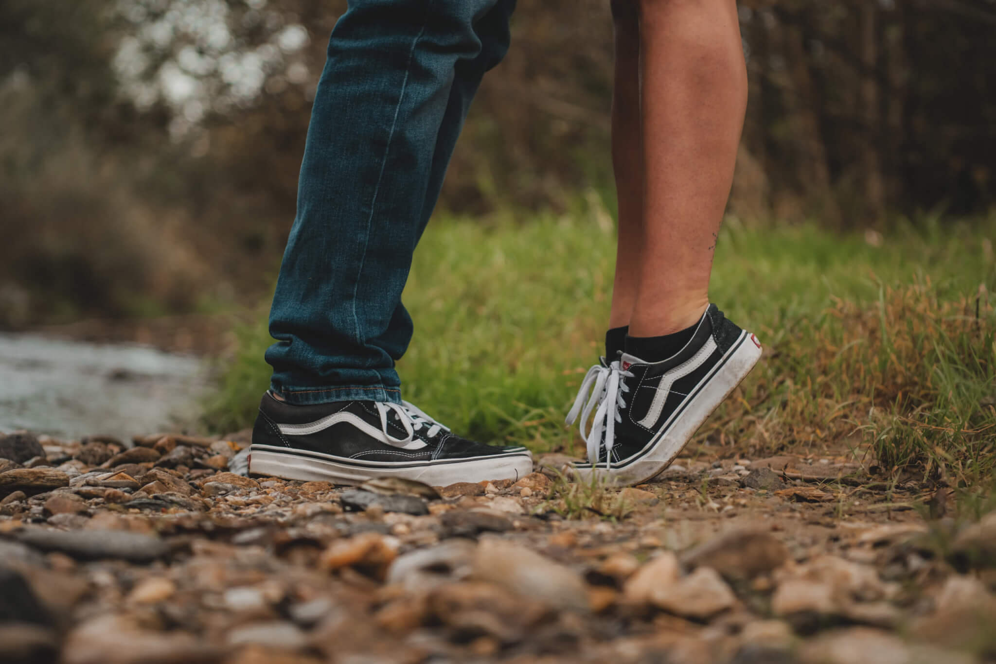 Zwei Personen stehen auf Schotterweg und tragen Vans-Schuhe, kniend für einen Kuss.