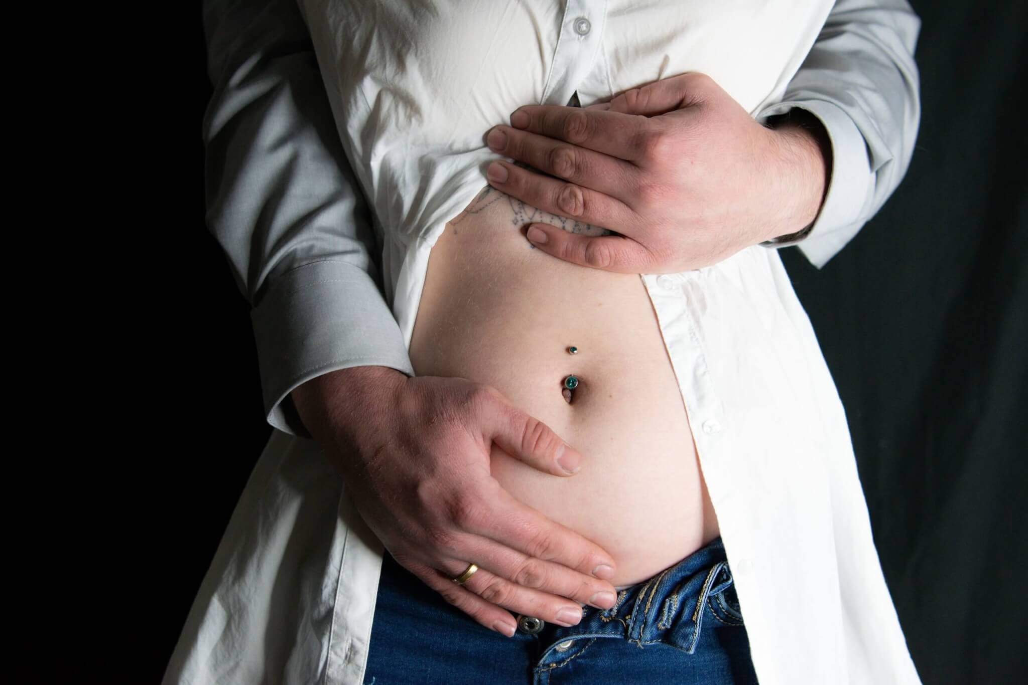 Hände auf einem Babybauch, Schwangerschaft, zukünftige Eltern, Bauchpiercing, emotionale Verbindung, Vorfreude auf das Baby.