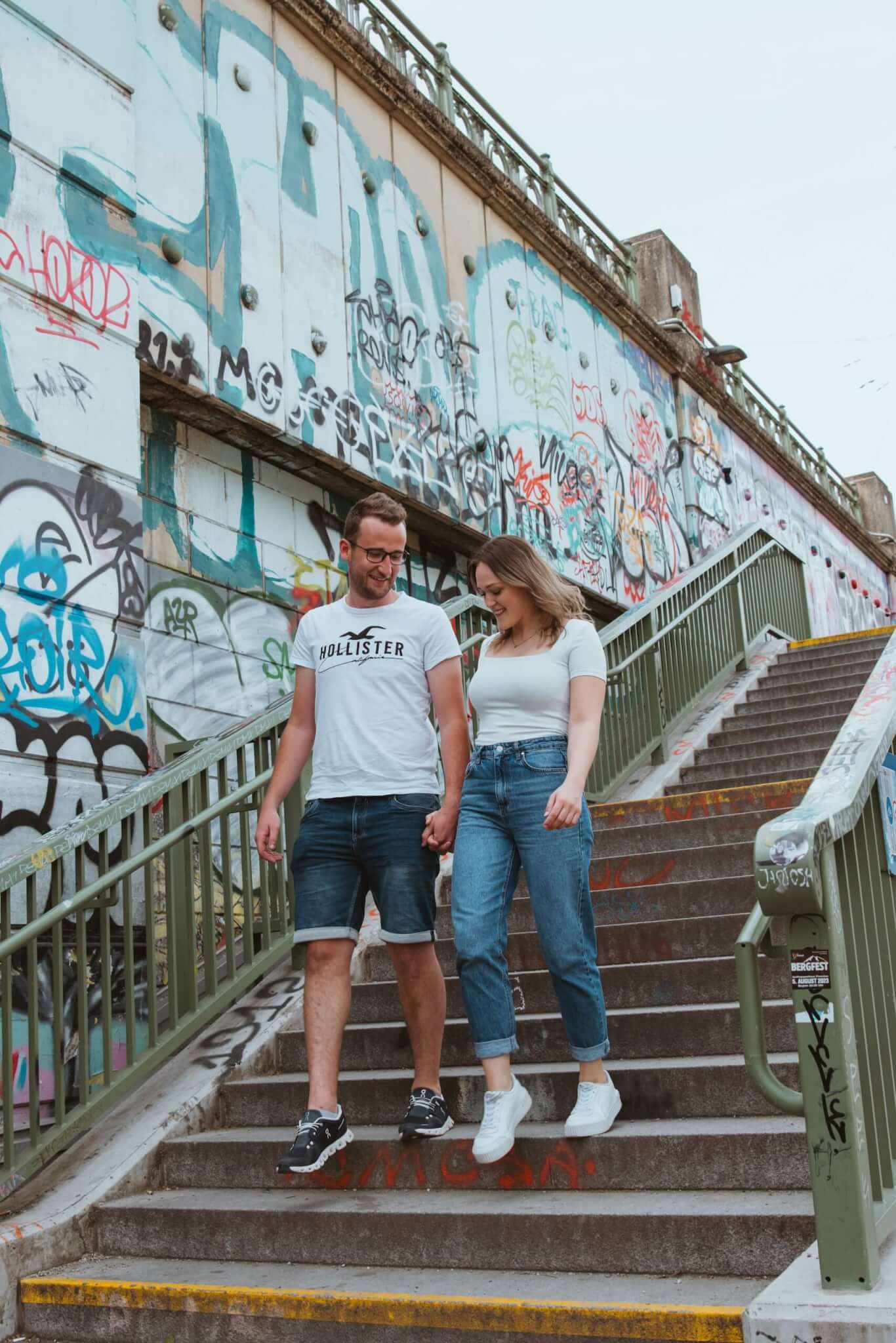 Paar geht Hand in Hand eine mit Graffiti bedeckte Treppe hinunter, urbanes Street-Art-Umfeld.