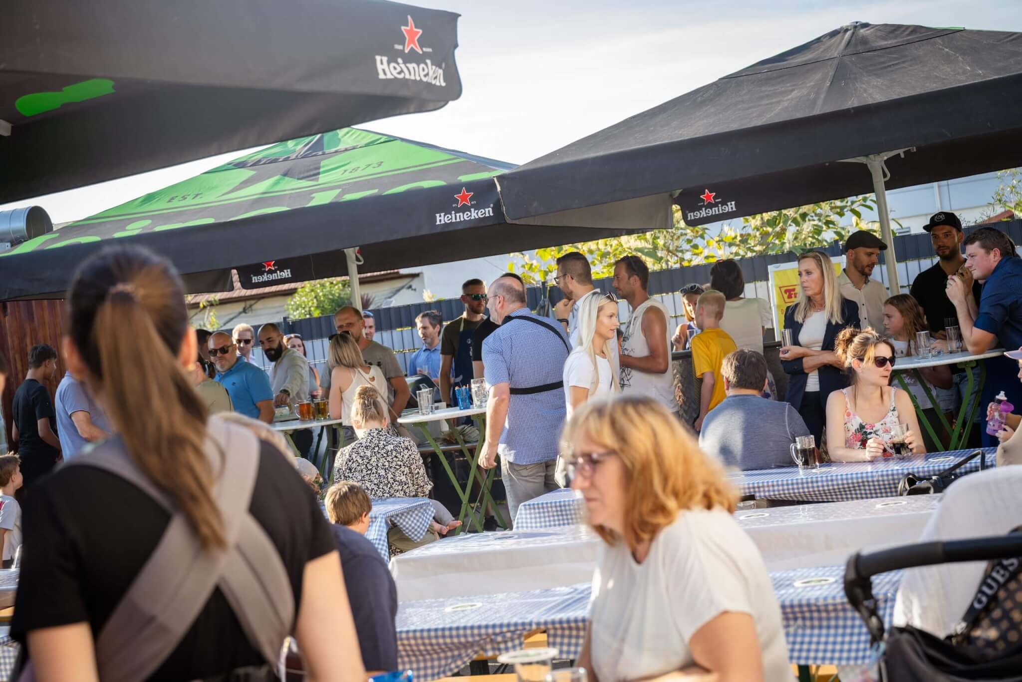 Menschen genießen eine Veranstaltung im Freien unter Heineken-Sonnenschirmen an einem sonnigen Tag.