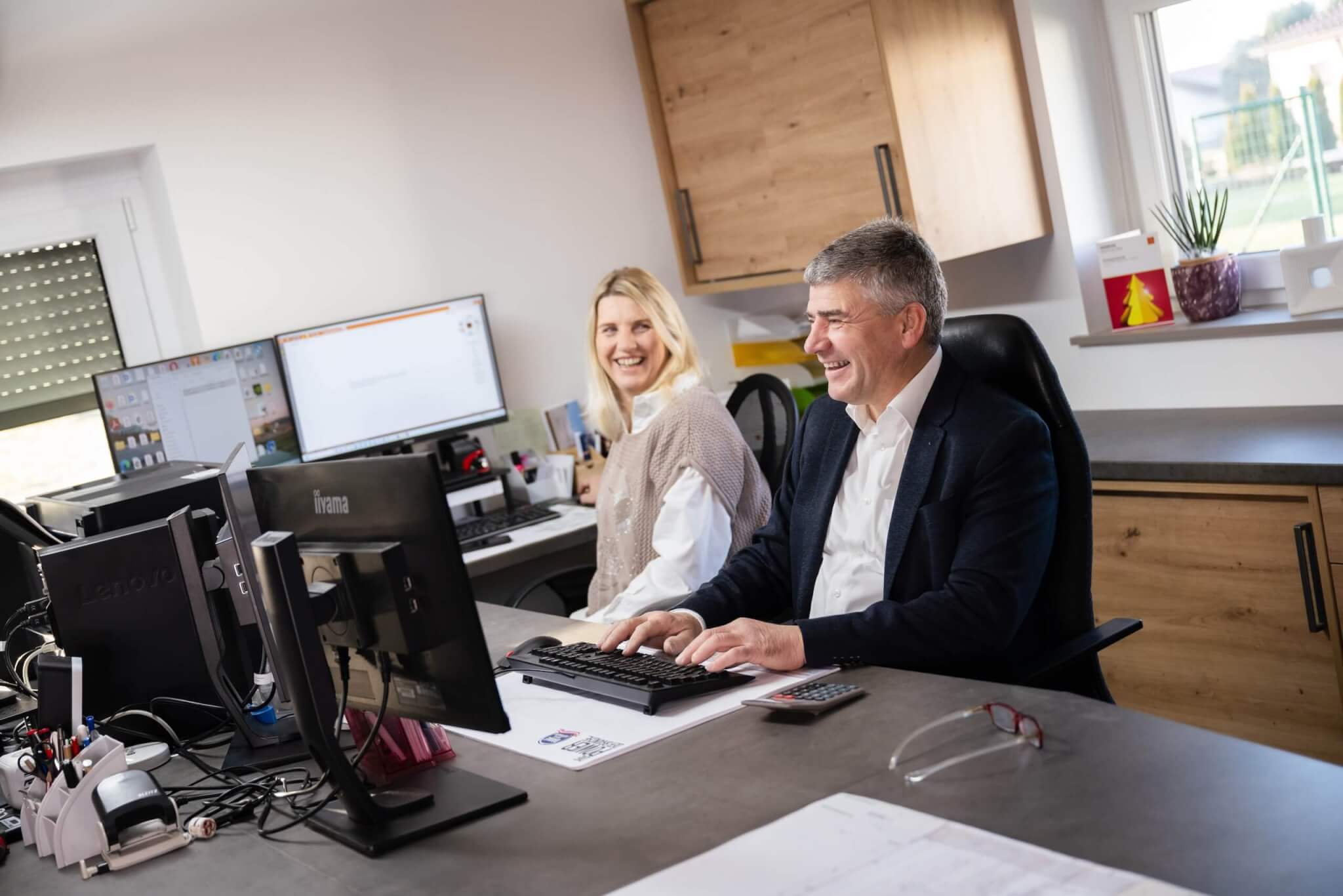 Lächelnde Büroangestellte arbeiten an Computern in modernem Büro, mit Monitoren und Bürozubehör.