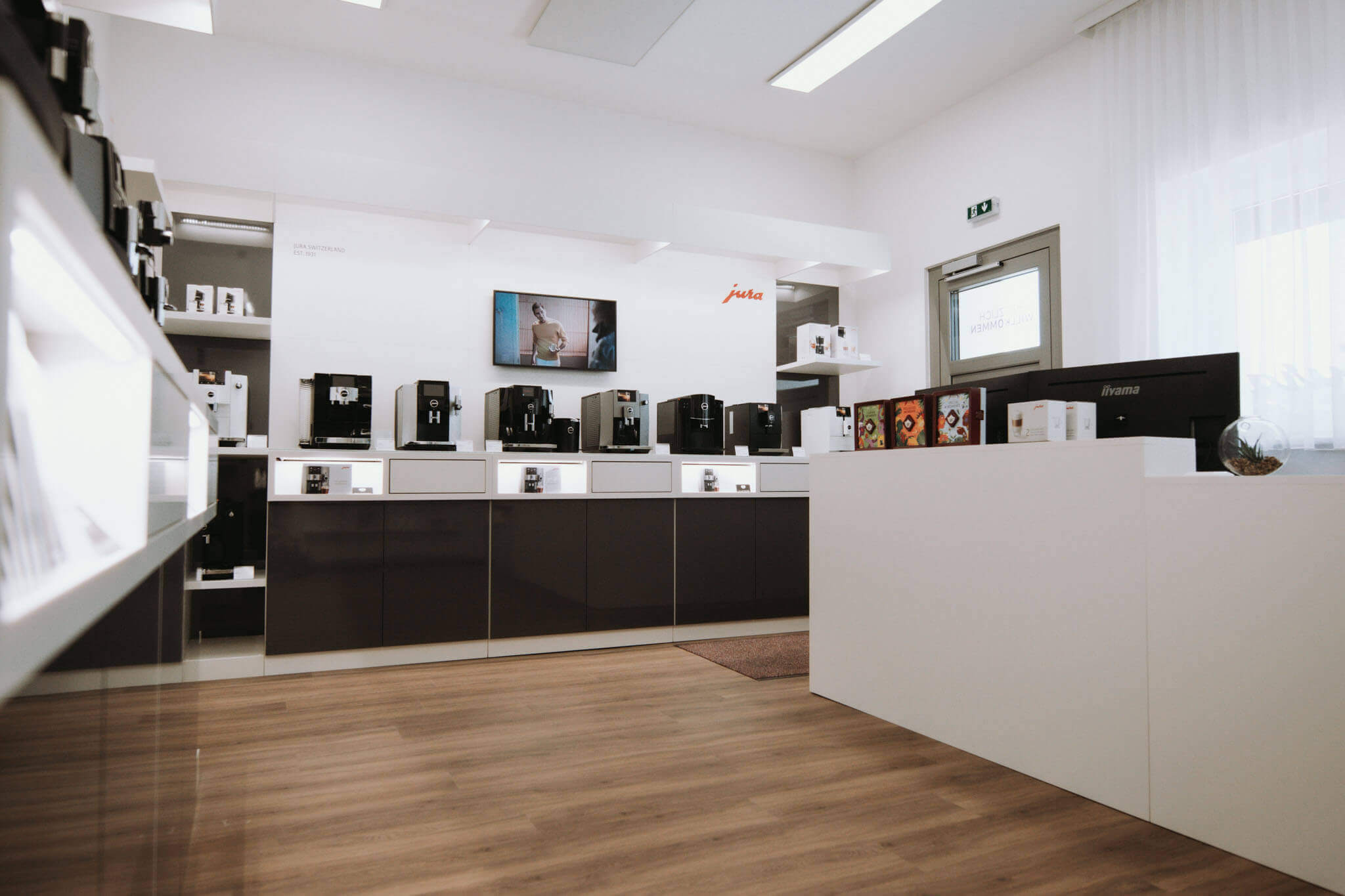 Moderner Showroom mit Kaffeemaschinen auf Verkaufstheke, elegantes Design und Holzfußboden.