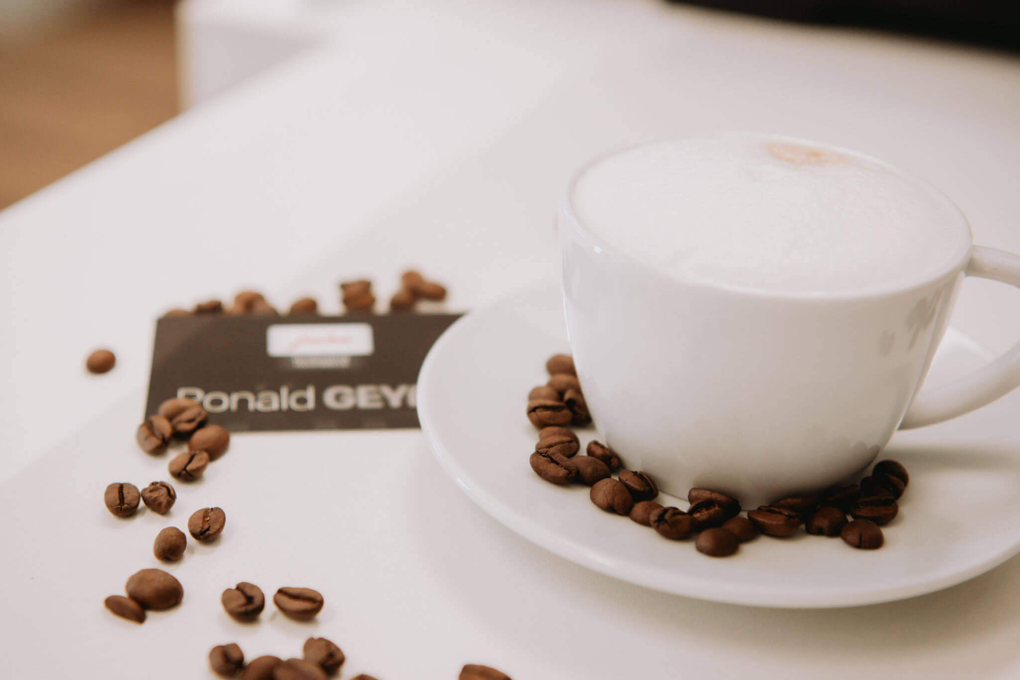 Tasse Cappuccino auf weißem Tisch, umgeben von Kaffeebohnen. Frisch zubereitetes Getränk für Kaffeeliebhaber.