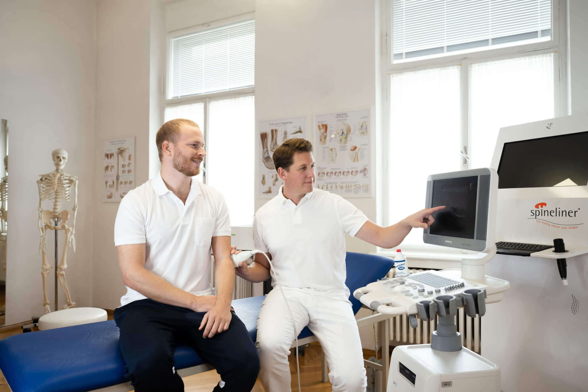 Chiropraktor erklärt mit Patient Behandlungsdetails auf einem Monitor in moderner Praxisumgebung.