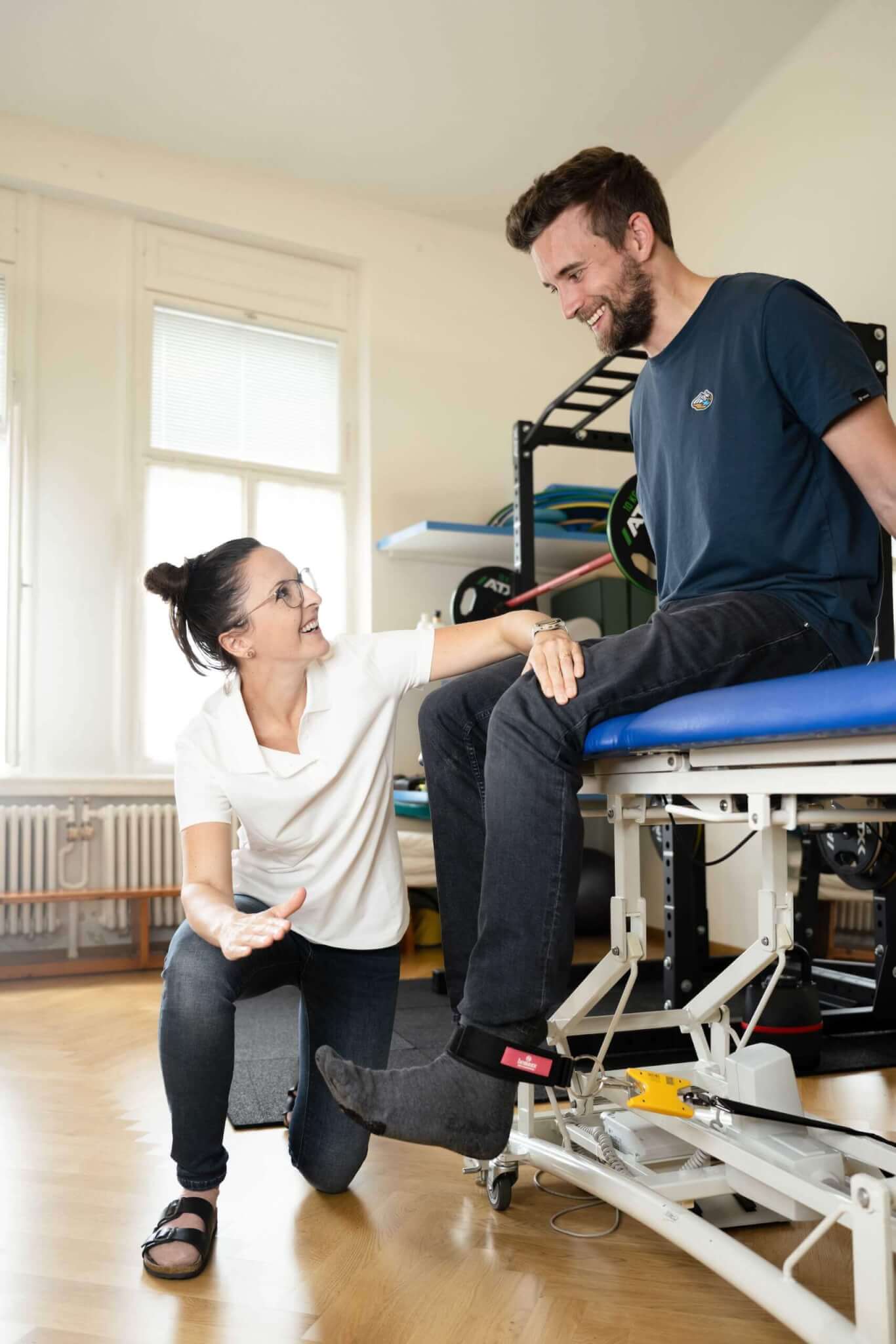 Physiotherapeutin behandelt Patient auf Rehabilitationsgerät im Therapieraum.