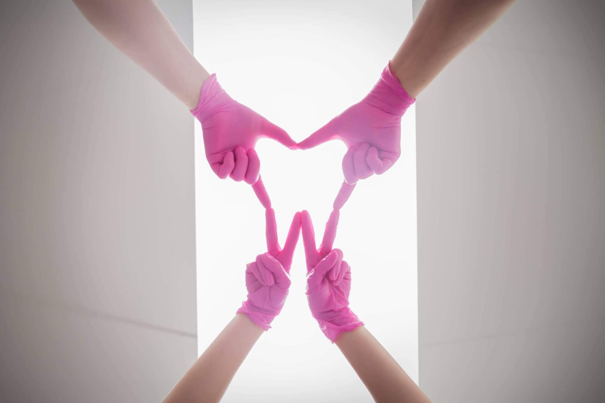 Hände in pinken Handschuhen formen ein Herz aus Fingern, symbolisieren Teamarbeit und Kreativität.